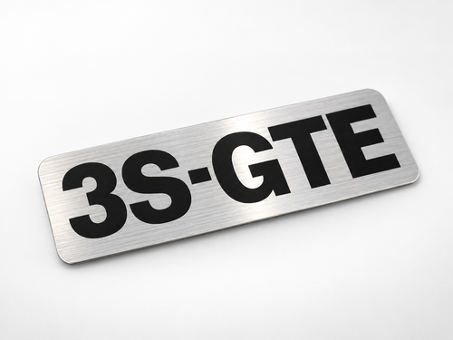 Silver reproduction 3S-GTE timing cover decal with black letters on brushed aluminum